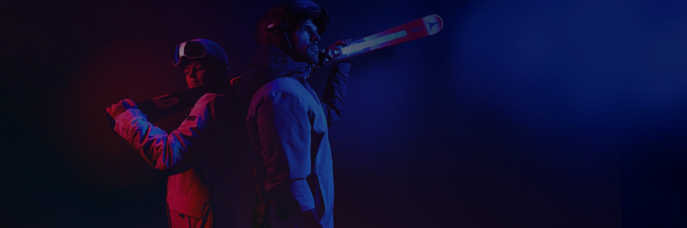 Zwei Skifahrer in Winterausrüstung stehen Rücken an Rücken, jeder hält die Skier über den Schultern. Das Bild verwendet dramatisches rotes und blaues Licht, das ihre konzentrierten Ausdrücke und ihre moderne Ausrüstung hervorhebt.