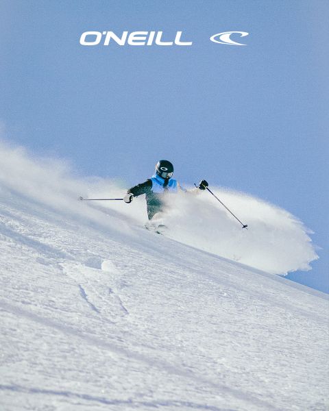 Eine Frau mit langen Haaren steht in einer Wüstenlandschaft unter einem blauen Himmel mit vereinzelten Wolken. Sie trägt ein schwarzes O'Neill-Tanktop und lehnt sich leicht nach vorne. Auf der rechten Seite des Bildes ist das O'Neill-Logo zu sehen.